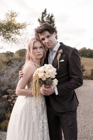 Brautpaar steht eng umschlungen mit Blumenstrauß im Garten